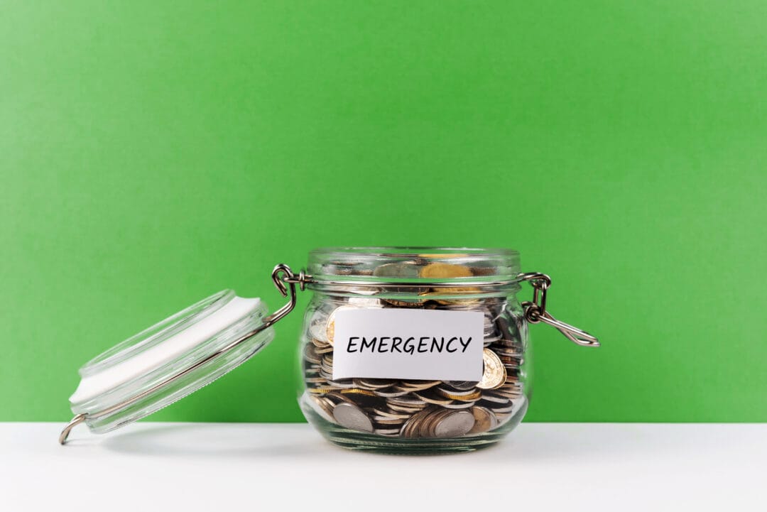 A jar containing coins, representing emergency savings, placed on a striking green background.