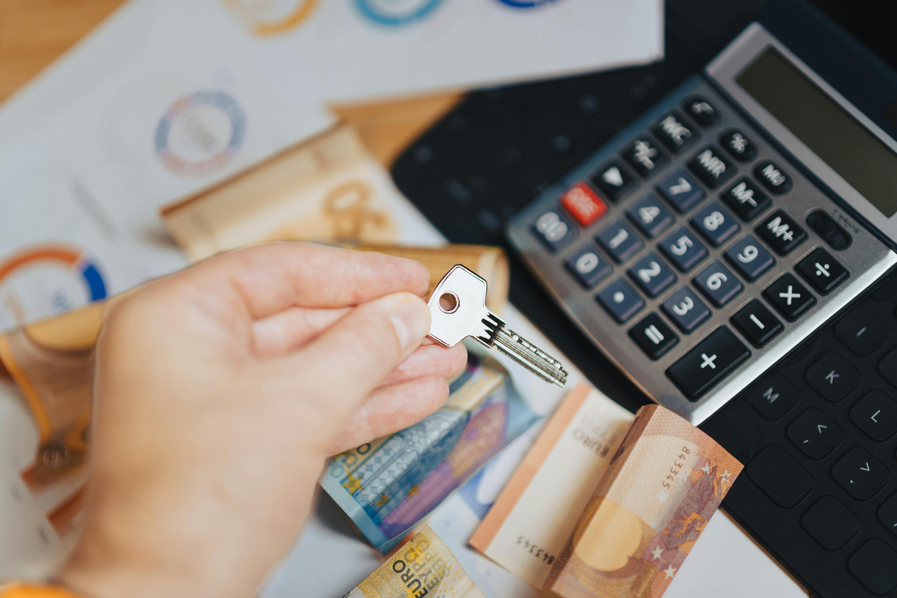  A hand holding a key, cash notes, and a calculator, symbolizing financial planning and budgeting.