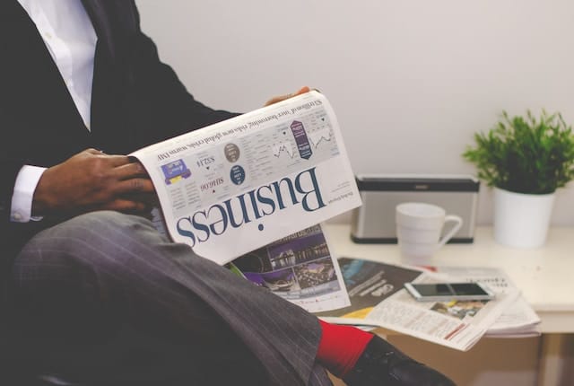 Man in a suit reading a business newspaper at his office desk.