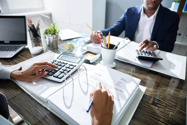 Office desk featuring a calculator, company stationery, a loan offer certificate, and hands typing on a calculater and taking notes.