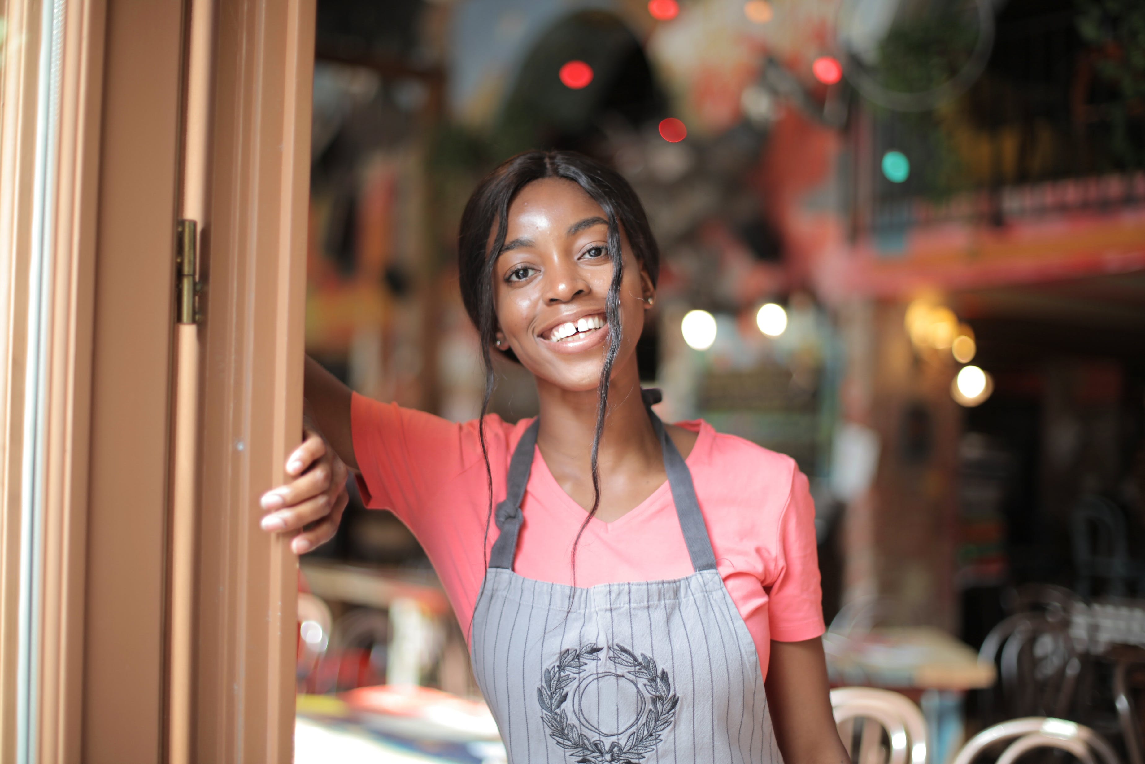 Black African woman smiling warmly at the entrance of her café business.