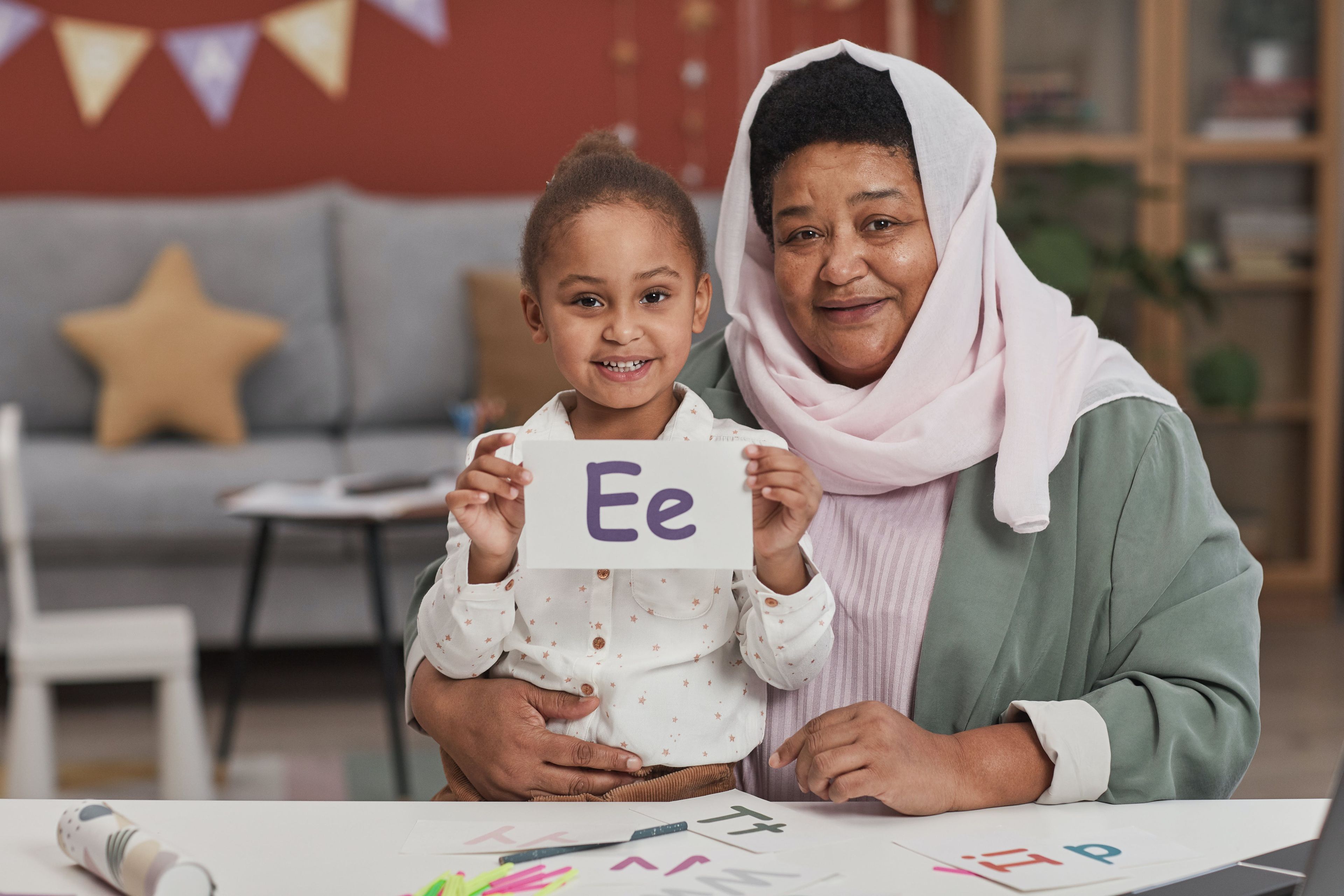 Grandmother and daughter proudly holding up a homework page featuring the letter 'Ee.